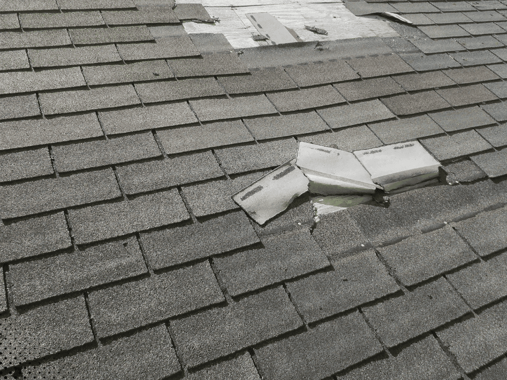 Loose and damaged roof shingles with displaced vent cover after wind damage in Idaho Falls home